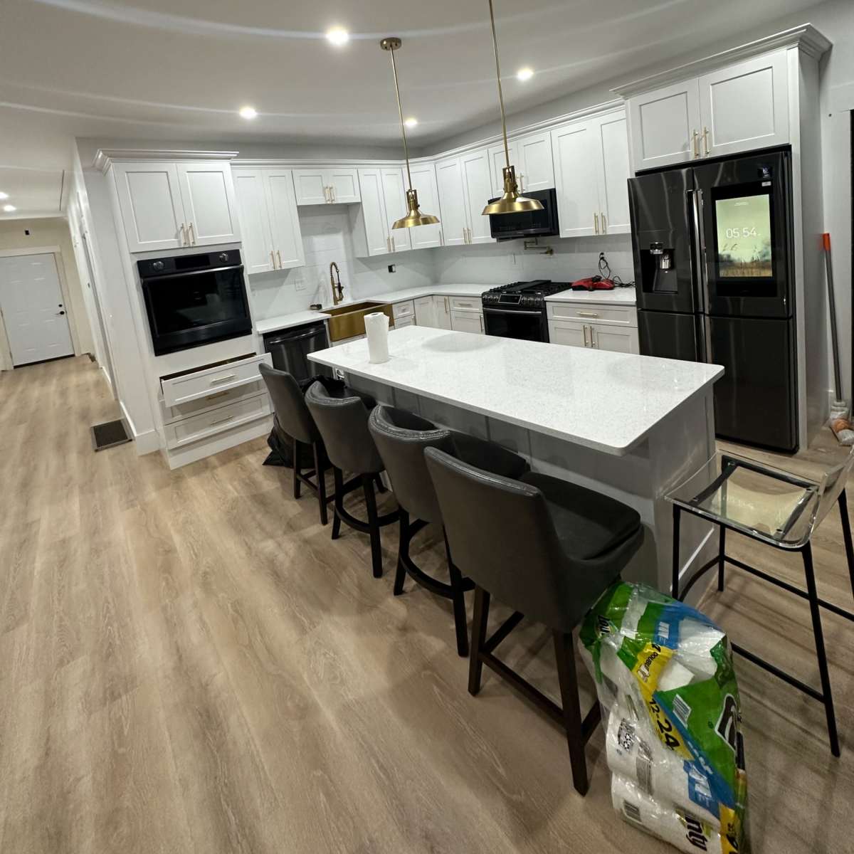 A modern kitchen features white cabinets, a central island with seating, and black appliances against a light wood floor.