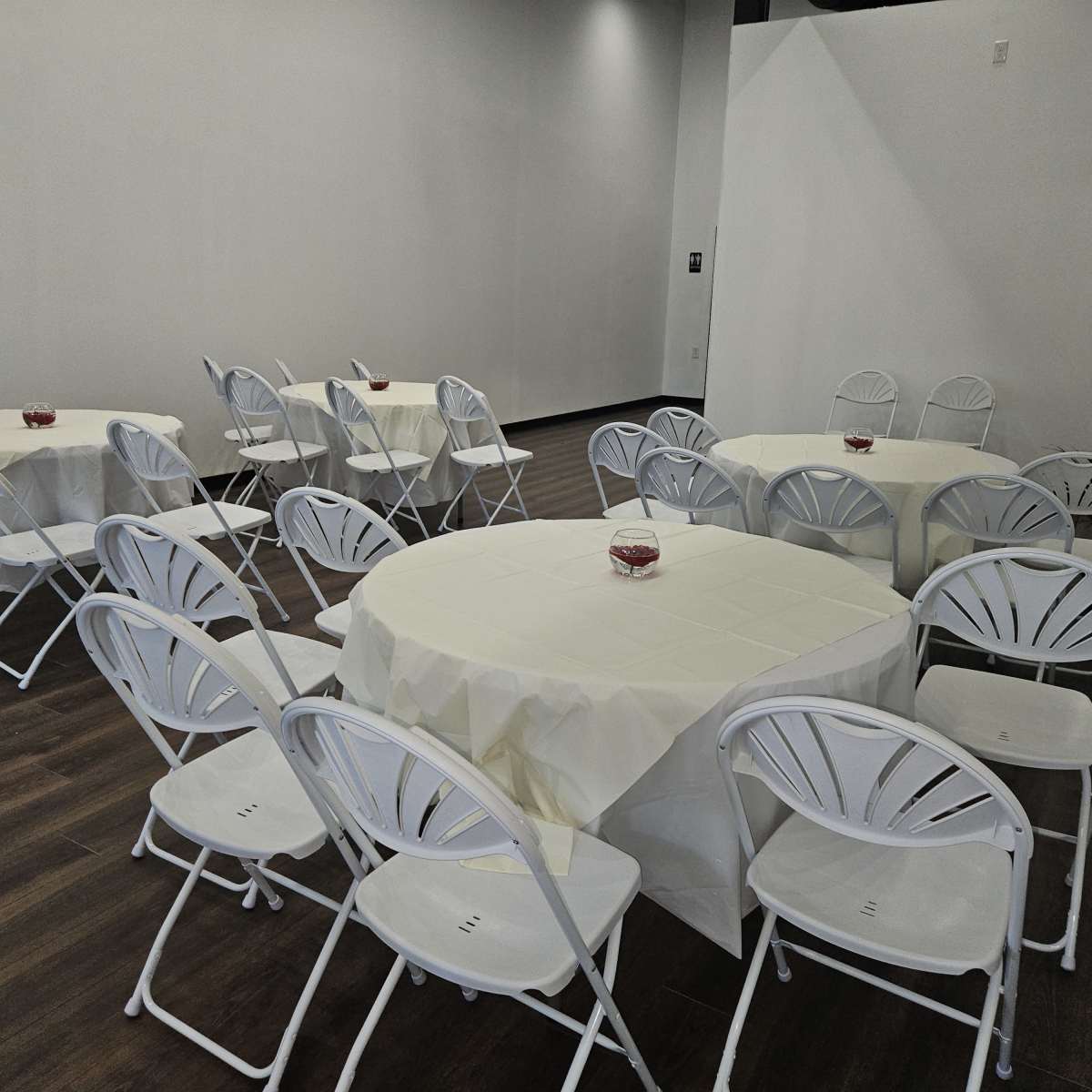 A room with several round tables covered with white tablecloths and surrounded by white folding chairs.
