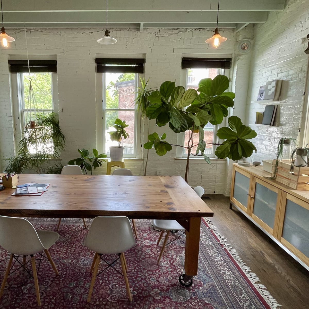 A bright, modern meeting room with a wooden table surrounded by chairs, large windows, and potted plants.
