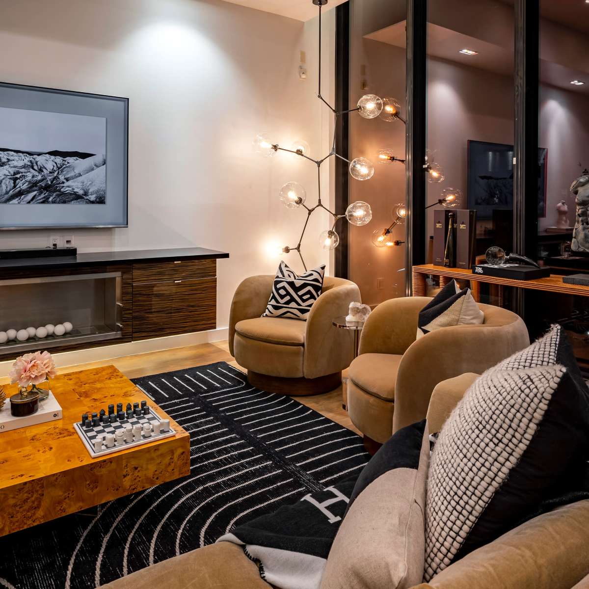 The living room features modern furniture, a large television on the wall, a stylish lighting fixture, and a chessboard on a wooden table.