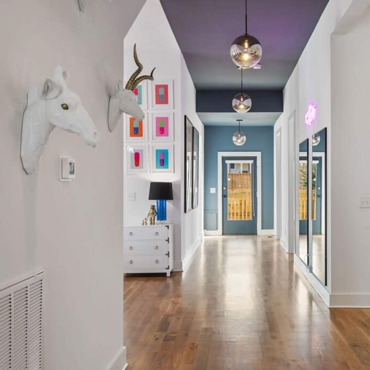 A bright hallway with dark blue walls, wooden flooring, and decorative items, including a unicorn head and a collection of colorful framed artworks.