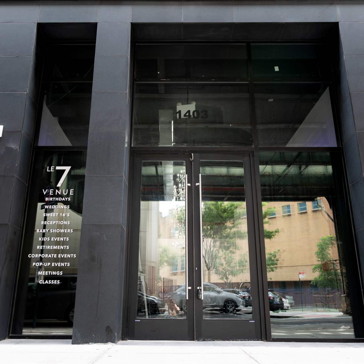 The entrance of a building with the name "LE 7" displayed on the glass door, along with various event services listed on the adjacent wall.