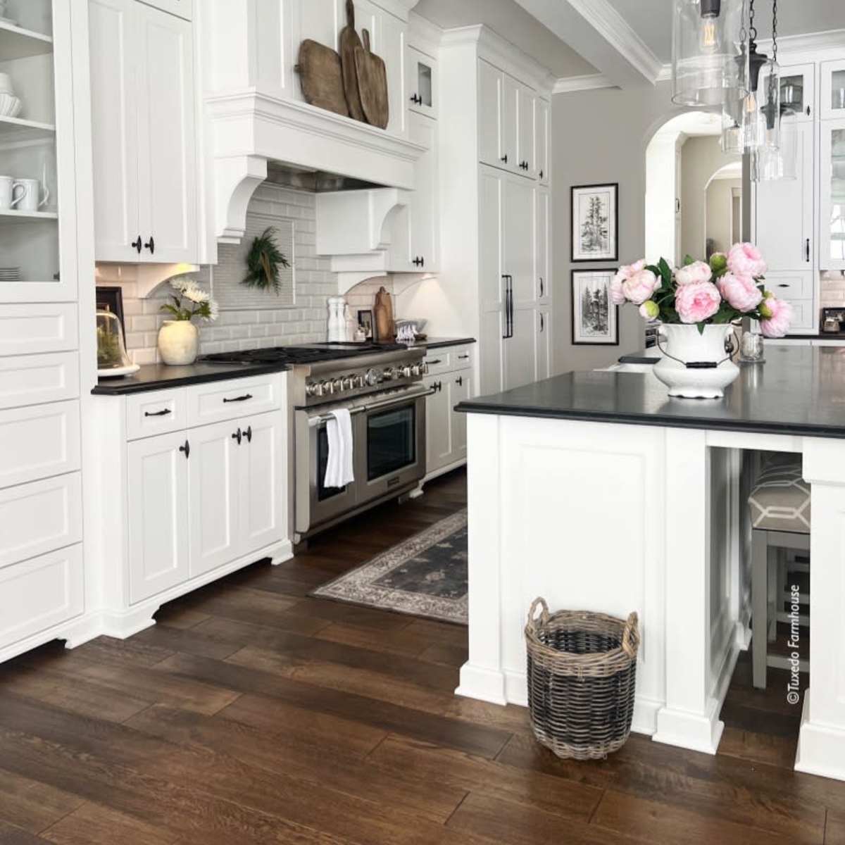 A modern kitchen featuring white cabinetry, a central island with a dark countertop, and stainless steel appliances, accented by pendant lighting and fresh flowers.
