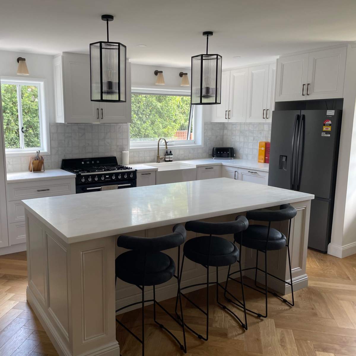 A modern kitchen featuring white cabinetry, a large island with bar stools, and a window allowing natural light to enter.