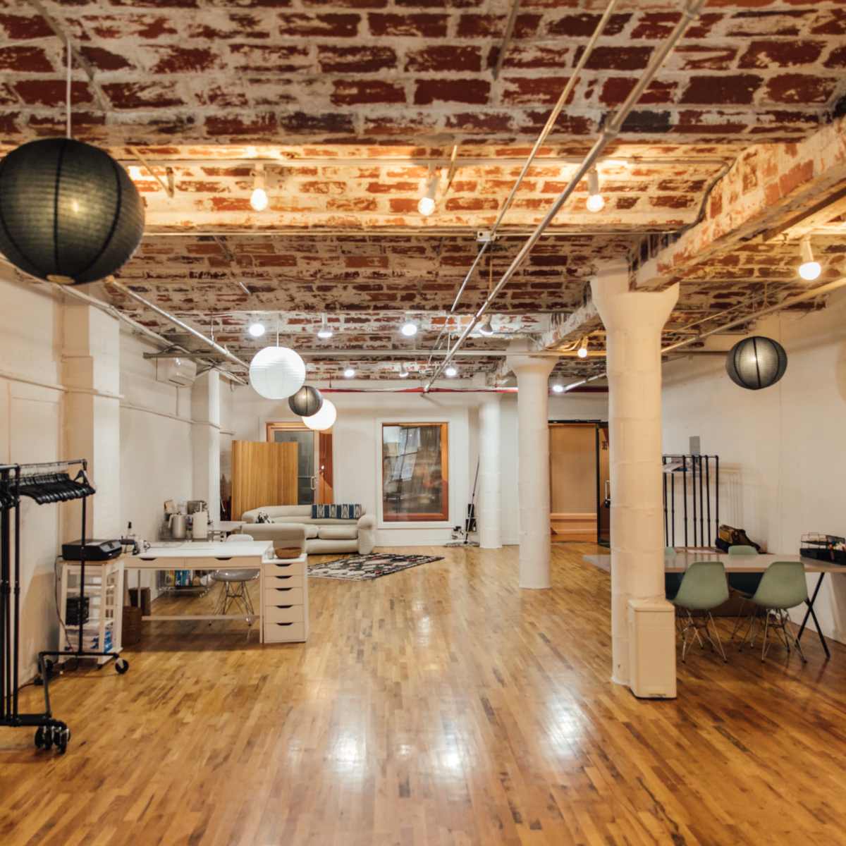 A spacious interior with exposed brick walls, wooden flooring, and various hanging lanterns, featuring furniture and equipment along the sides.