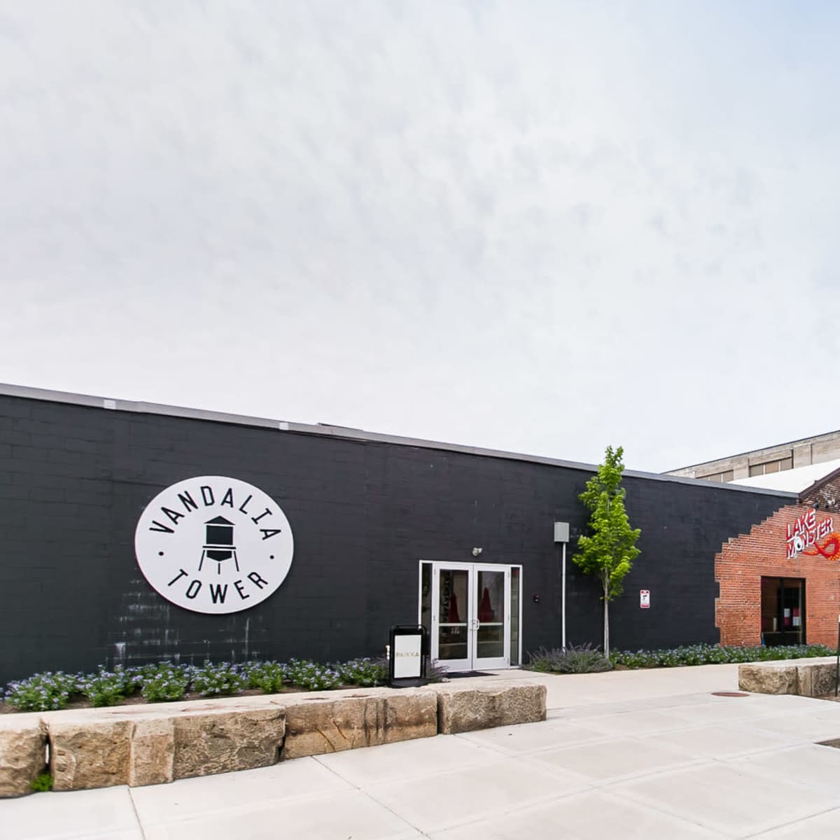 The exterior of a building labeled "Vandalia Tower," featuring a modern design with outdoor seating and red umbrellas.