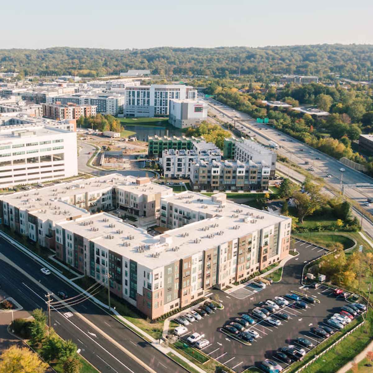 An aerial view of a modern urban area featuring residential and commercial buildings, green spaces, and roadways.