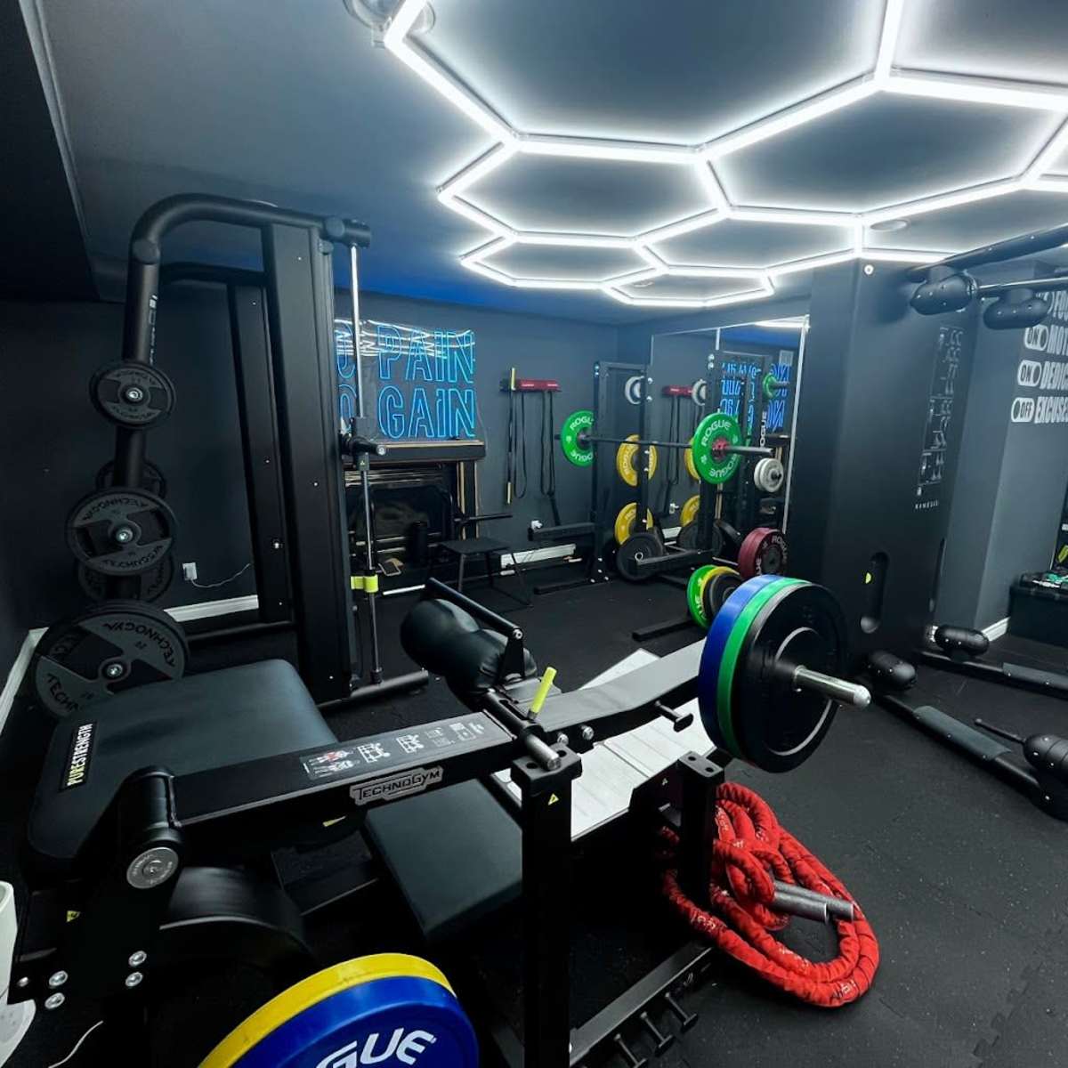A modern gym interior with various weightlifting equipment, including a bench press and free weights, illuminated by hexagonal LED lights.