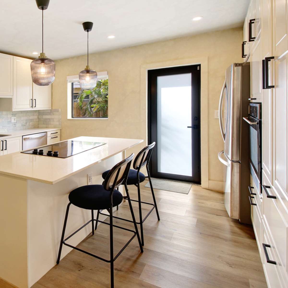 A modern kitchen with white cabinets, a central island with bar stools, and a sliding door leading to an outdoor area.