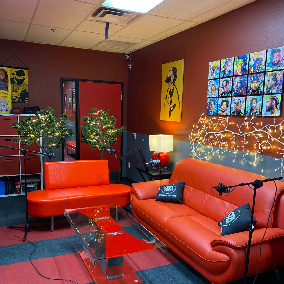 A recording studio with red walls, orange furniture, decorative lighting, and microphones set up for a podcast.