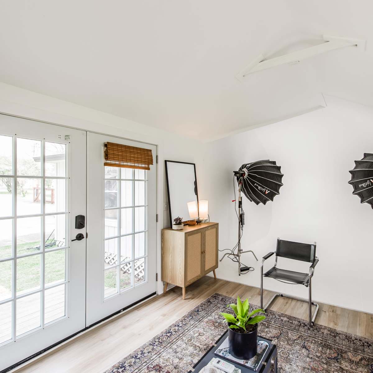 A photo studio with two lighting setups, a chair, a cabinet, a mirror, and glass doors leading to an outdoor area.
