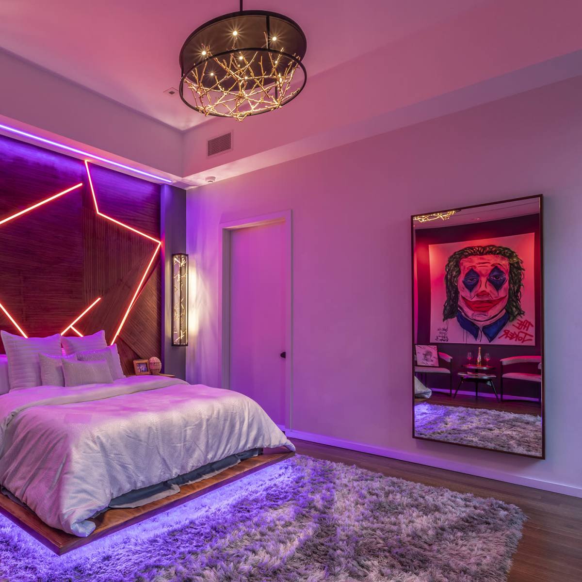A modern bedroom with a large bed, purple ambient lighting, and a mirrored wall displaying artwork.
