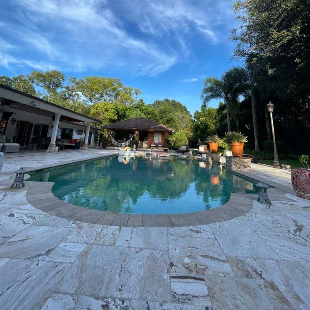 A swimming pool surrounded by lush greenery and a spacious outdoor area with a covered pavilion.