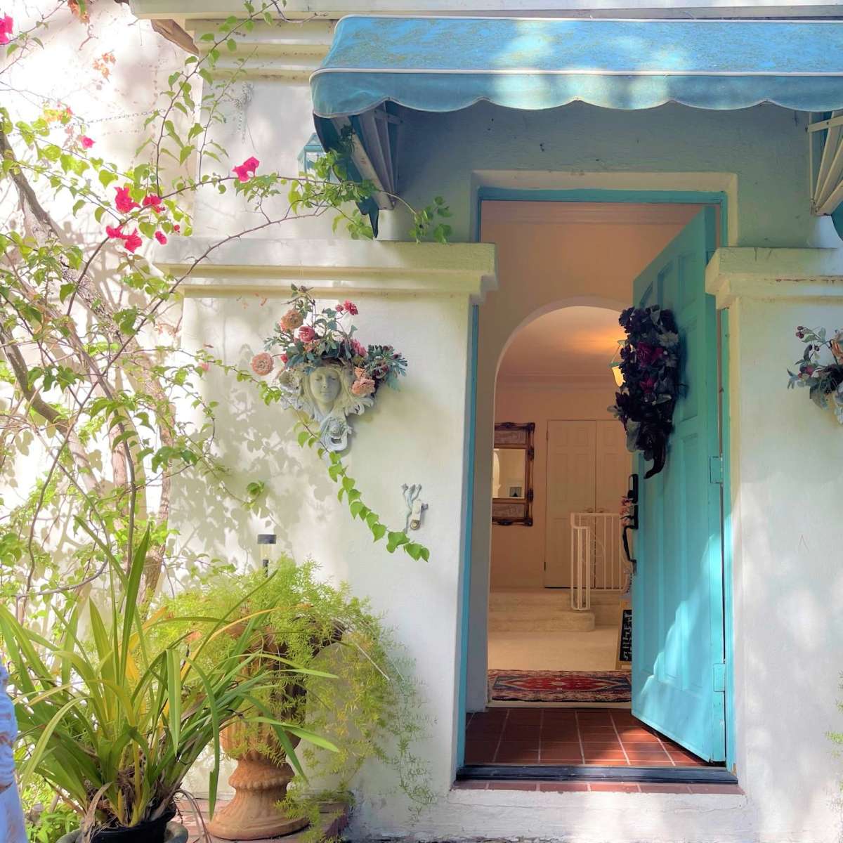 An inviting entrance with a light blue door framed by potted plants and floral decorations on either side.