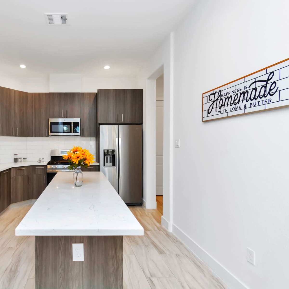 A modern kitchen with dark wood cabinetry, a white marble countertop, and stainless steel appliances, featuring a bouquet of flowers on the countertop.
