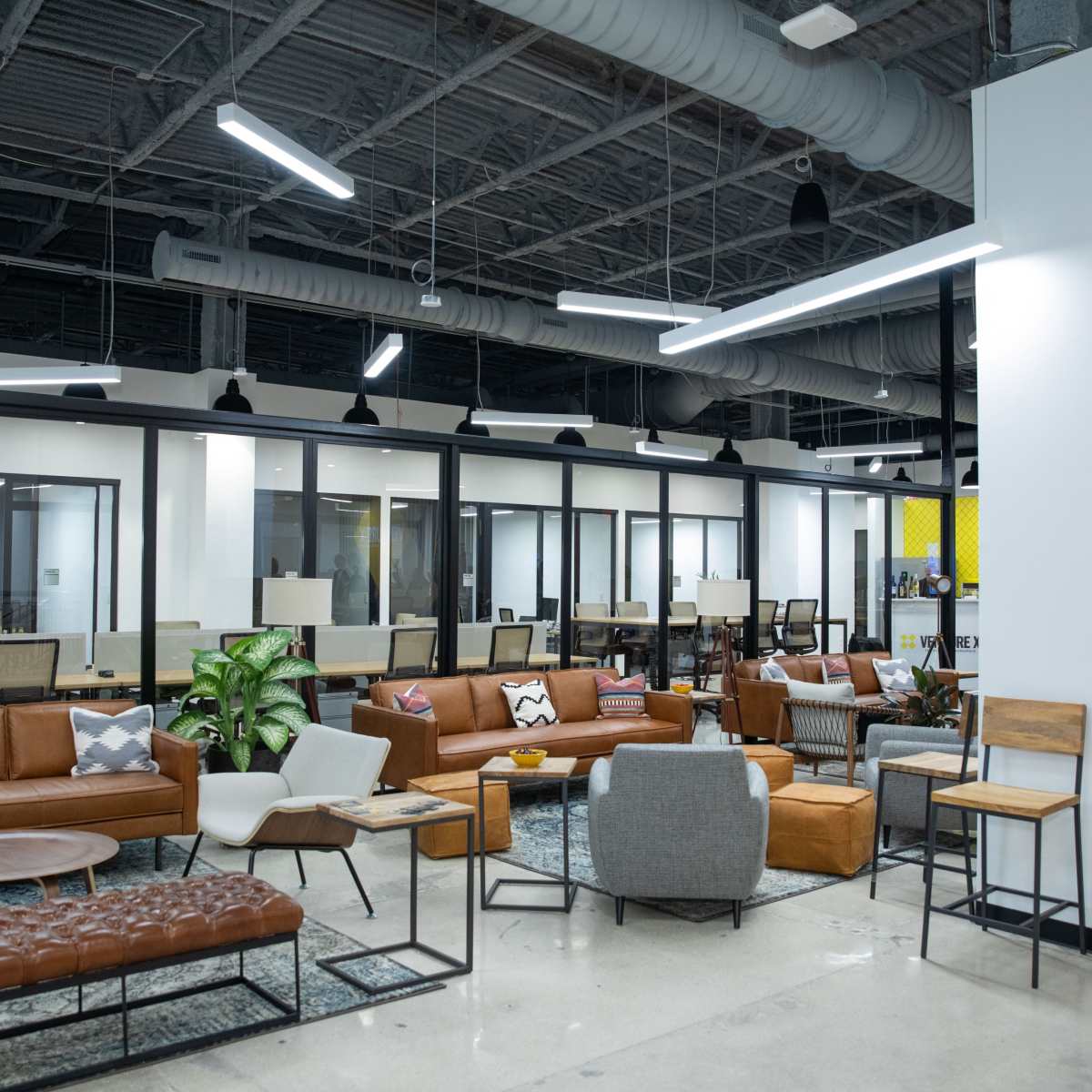 A modern office space featuring brown leather sofas, sleek furniture, and glass-walled meeting rooms.