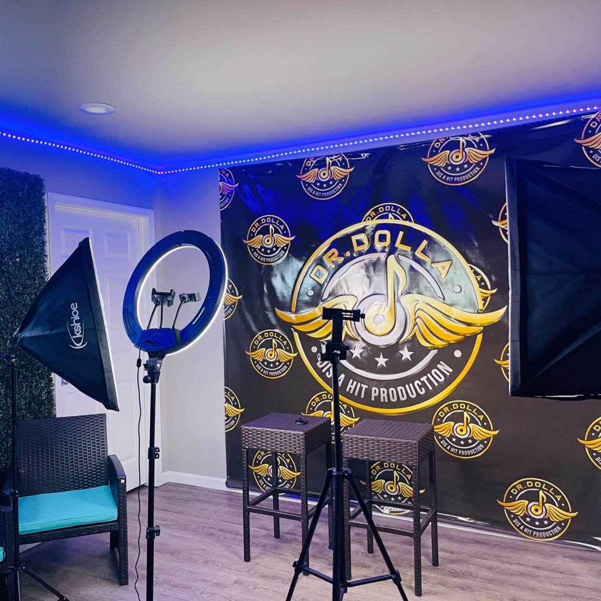A recording studio setup with lighting equipment, two chairs, and a branded backdrop featuring a logo.
