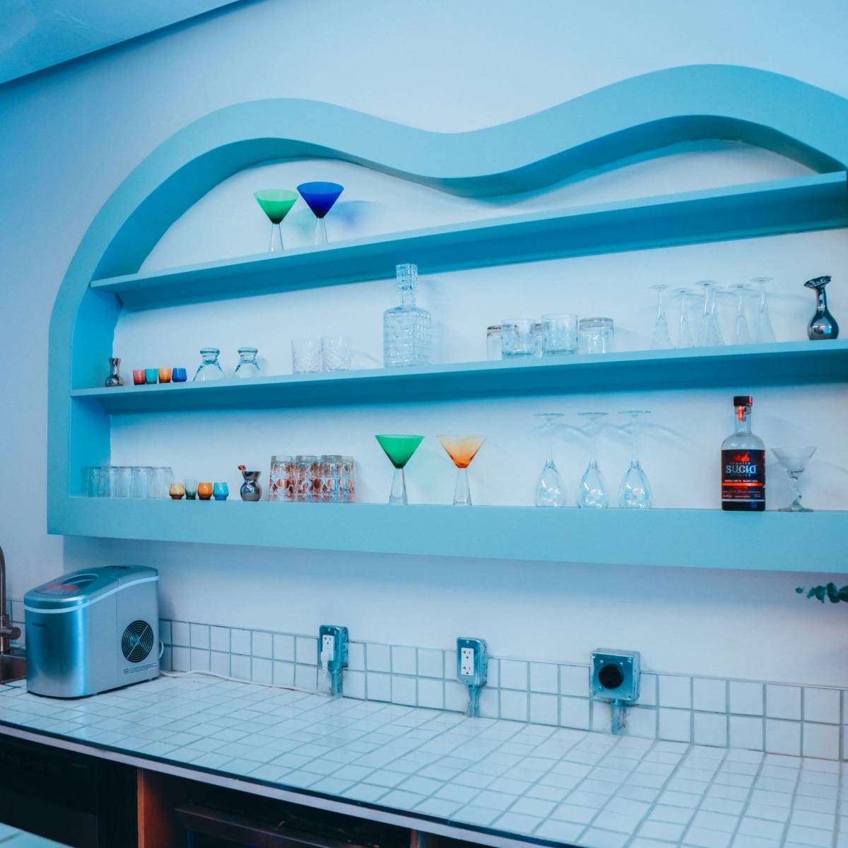A modern kitchen with a blue wavy shelf displaying various glassware and a small plant on the counter.