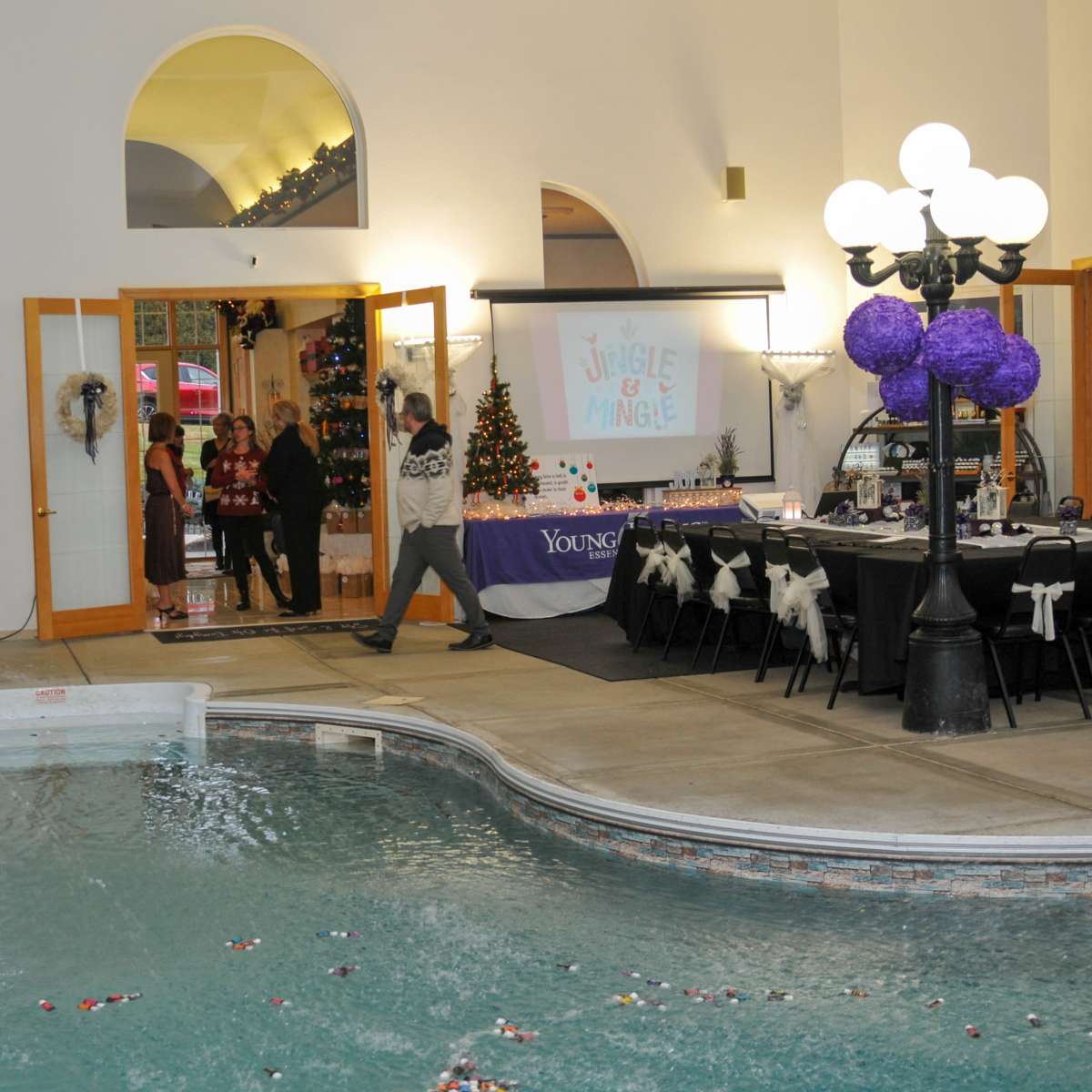 A festive indoor event takes place near a swimming pool, featuring musicians and a decorated dining area.