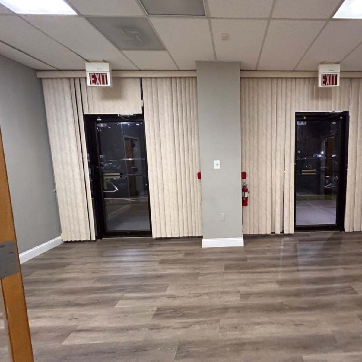 An empty room with two glass doors flanked by vertical blinds and a wooden floor.