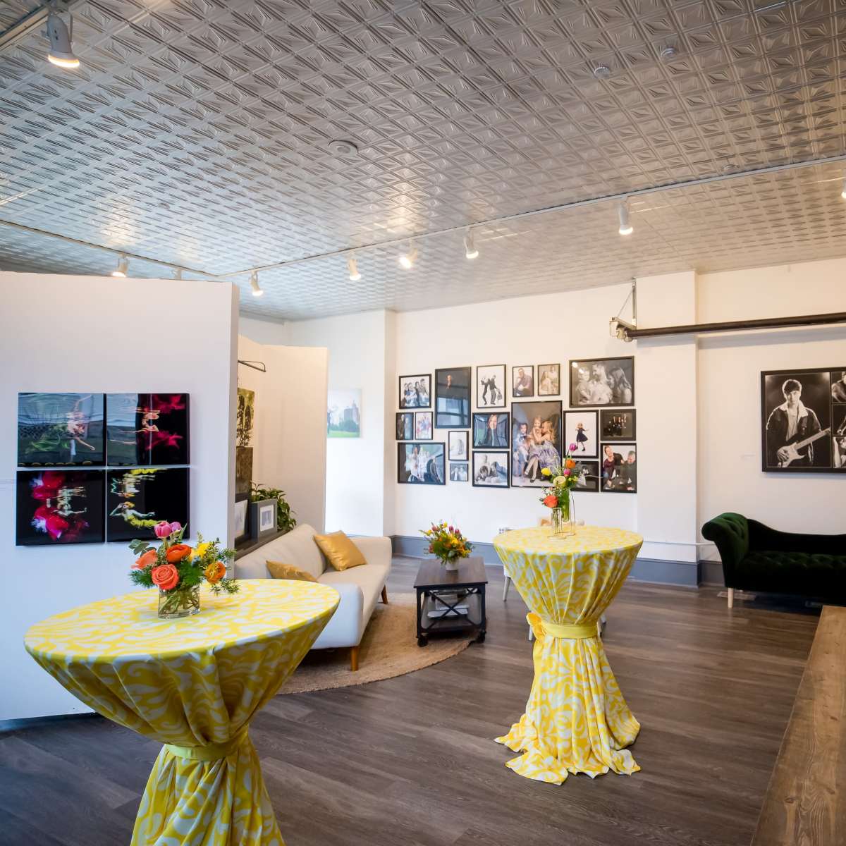 A spacious gallery with two yellow tables set with flowers, surrounded by framed photographs on the walls.