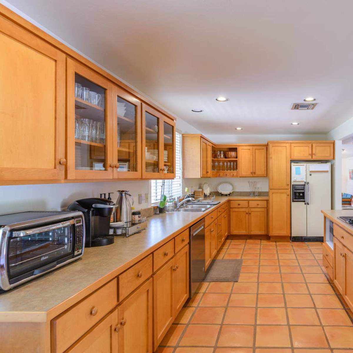 The kitchen features wooden cabinetry, a tile floor, and modern appliances arranged along long countertops.