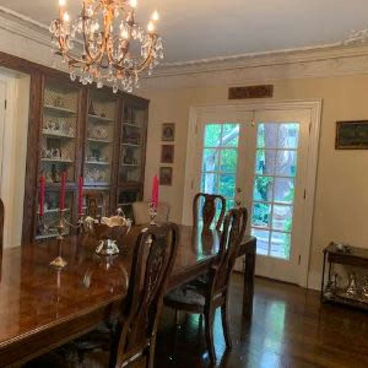 A dining room with a wooden table, several chairs, a chandelier, and a glass cabinet displaying decorative items.
