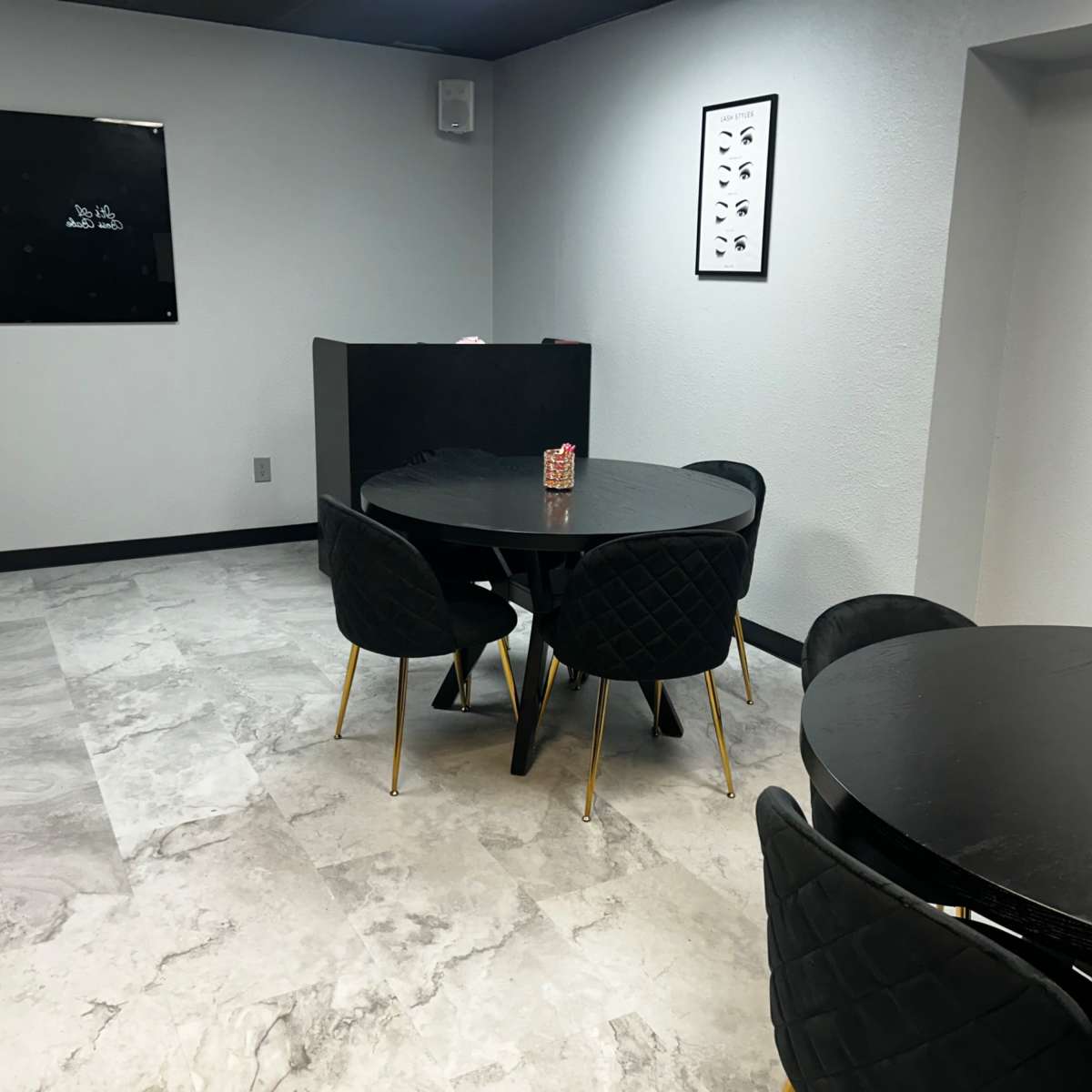 A modern, minimalist room featuring two round black tables surrounded by black chairs, with gray tile flooring and light walls.