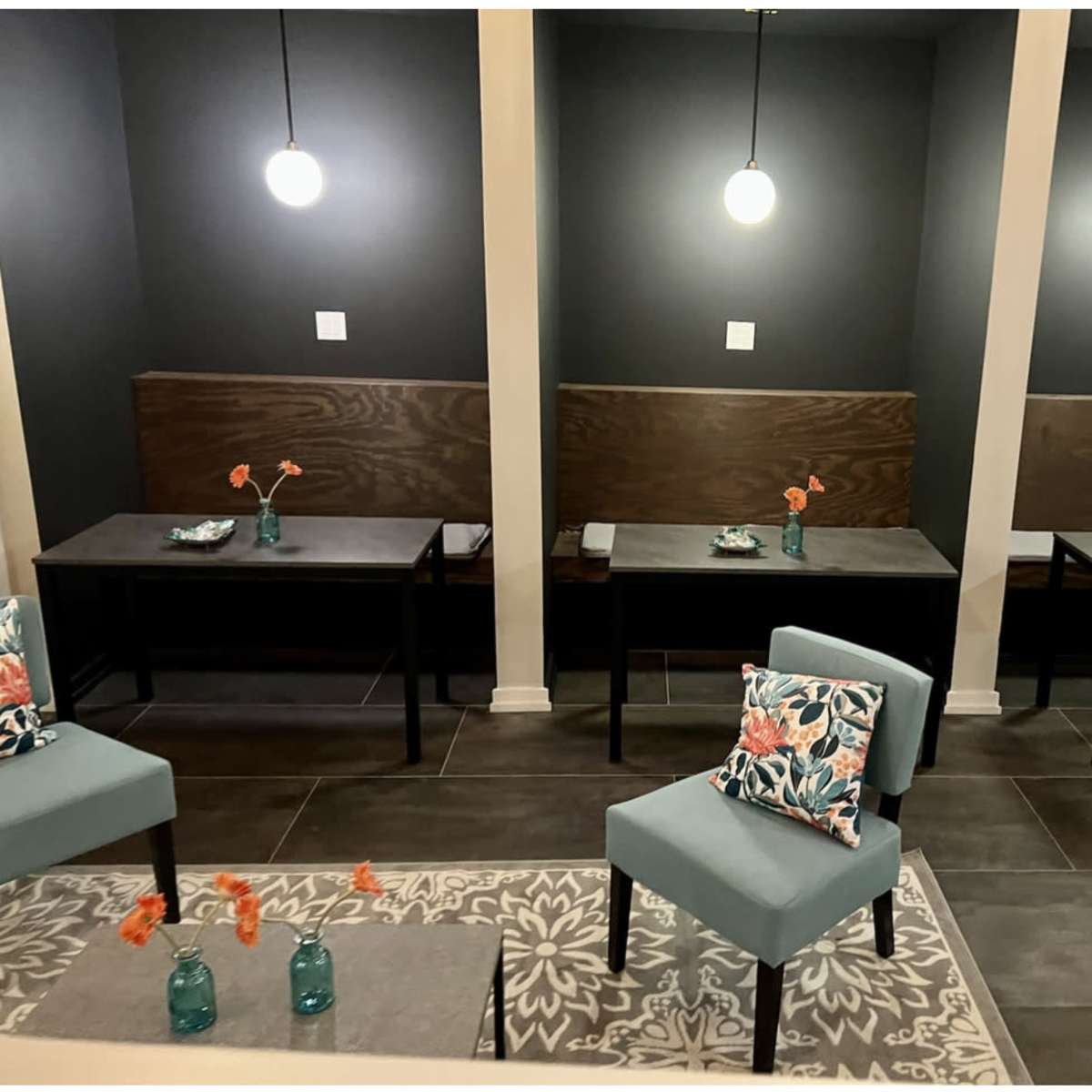 Three tables with chairs arranged in a dimly lit seating area featuring dark walls and pendant lighting.
