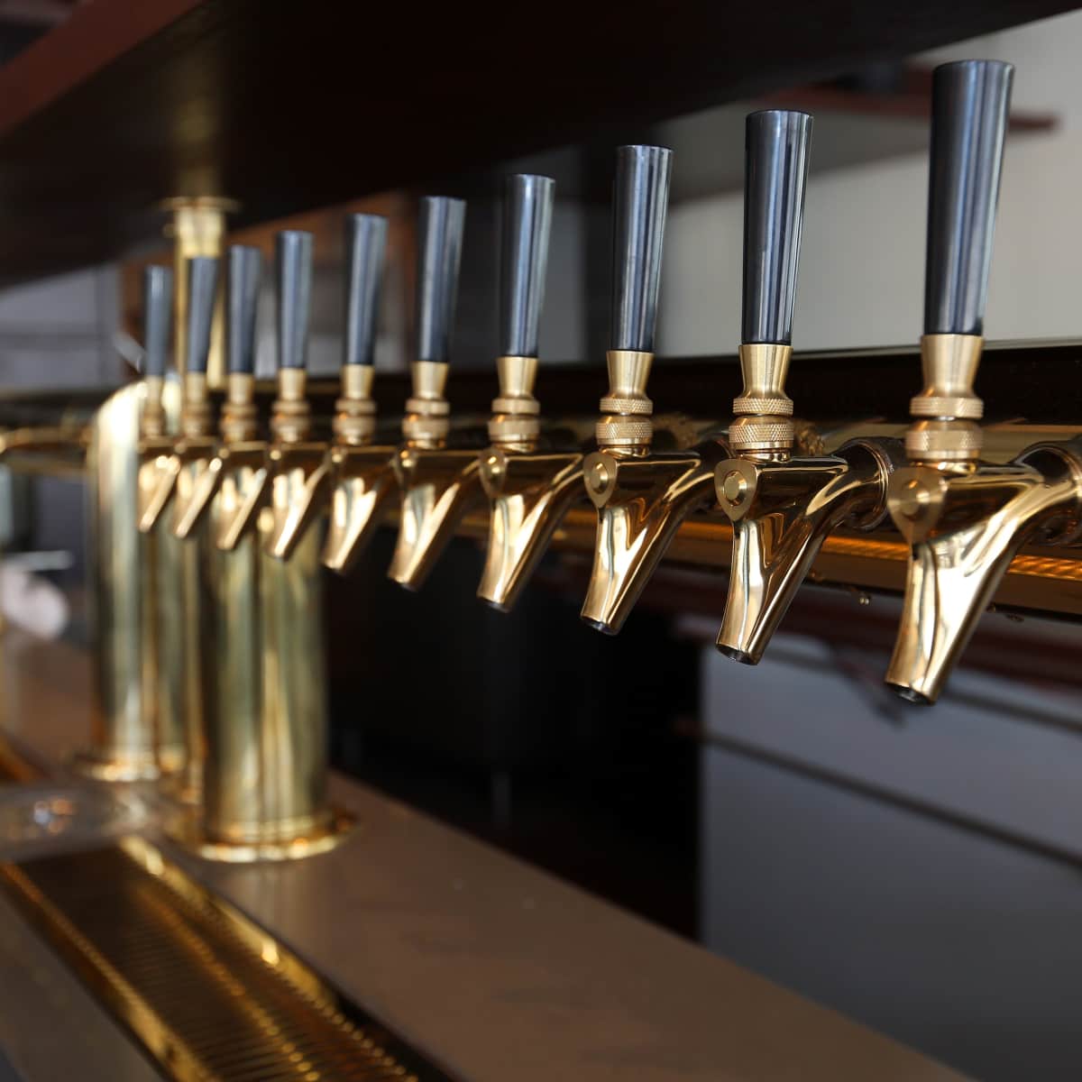 A row of polished brass beer taps arranged on a bar counter.