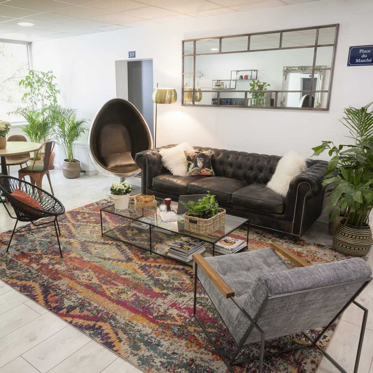 A cozy lounge area features a black leather sofa, a glass coffee table with plants, and various seating arrangements around a colorful rug.