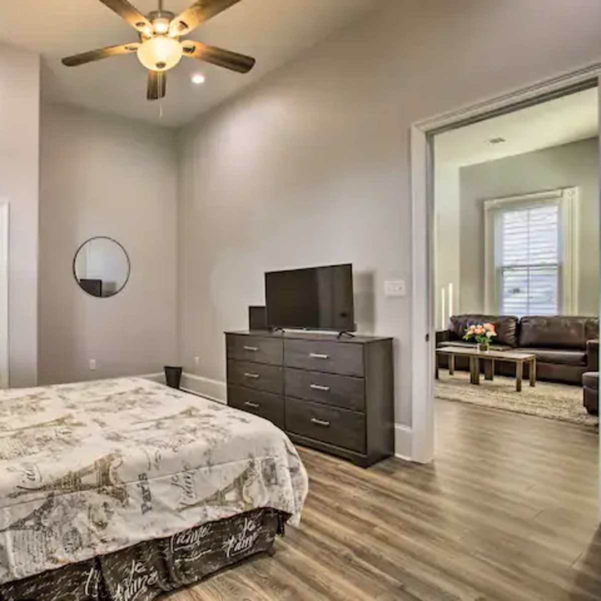 A bedroom with a bed, dresser, television, and a door leading to another room.