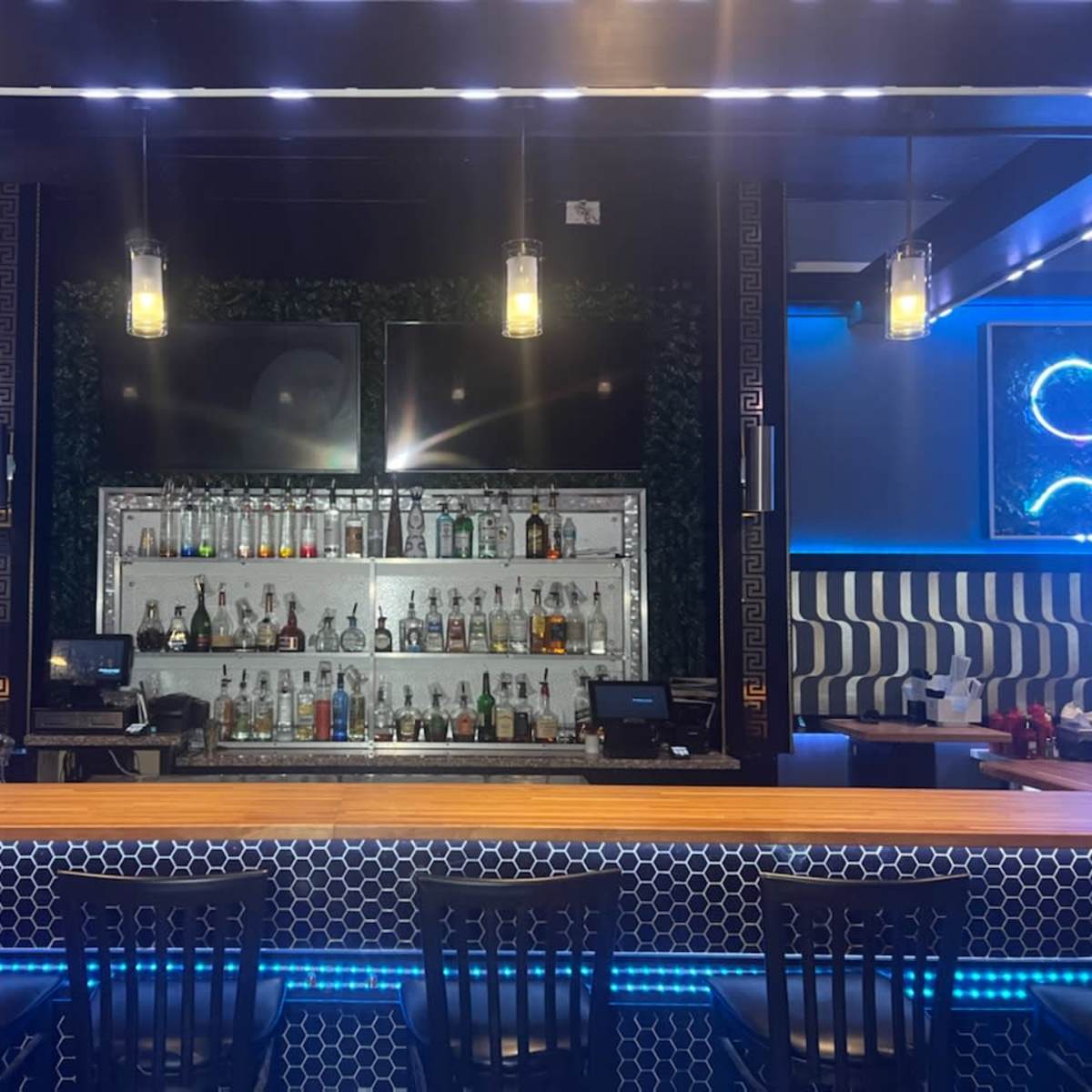 A modern bar with shelves of various liquor bottles illuminated by blue LED lights, set against a patterned wall.