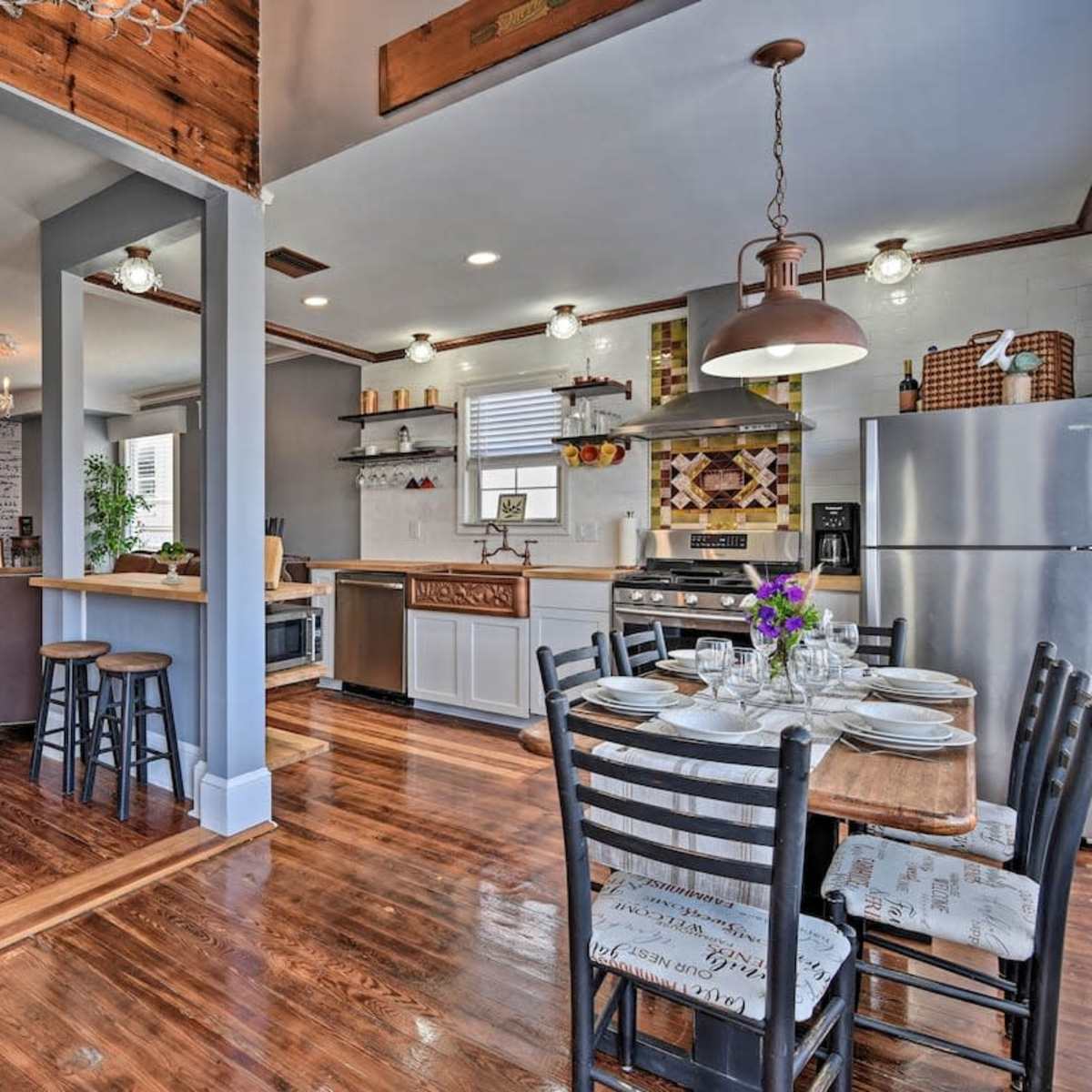 A modern kitchen and dining area with wooden flooring, a dining table set for six, and stainless steel appliances.