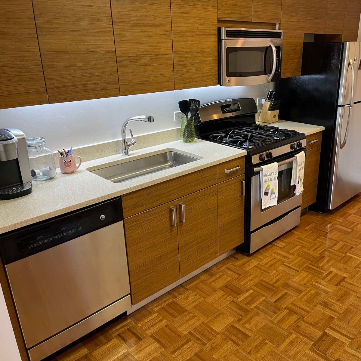 A modern kitchen with stainless steel appliances, including a stove, microwave, dishwasher, and refrigerator, set against wood panel cabinetry and a light countertop.