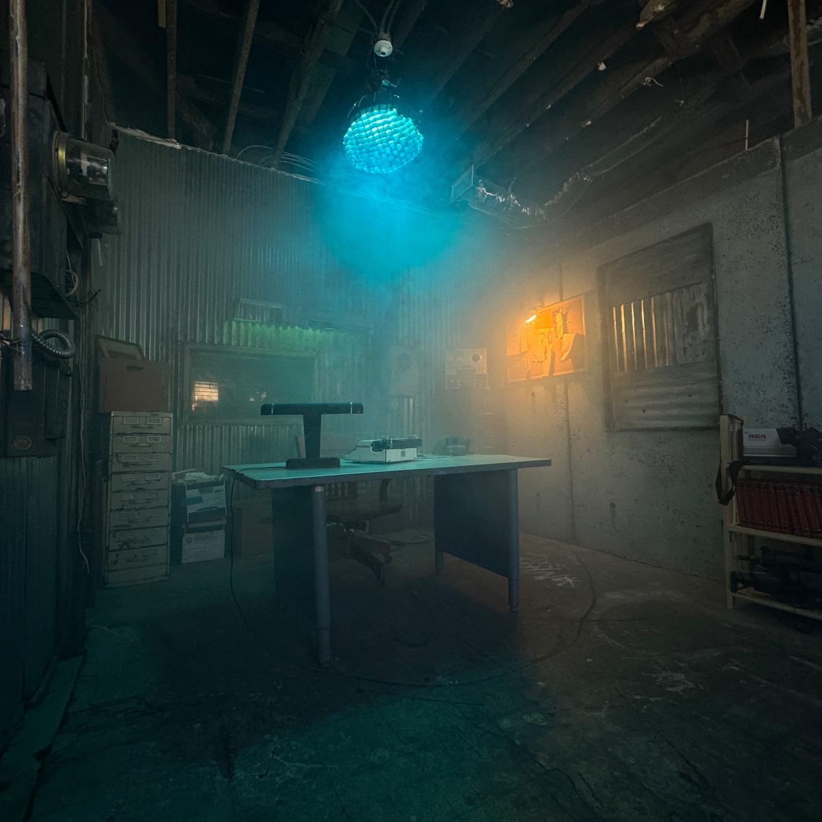A dimly lit room with a table in the center, surrounded by smoky air, metal walls, and a disco ball hanging from the ceiling.