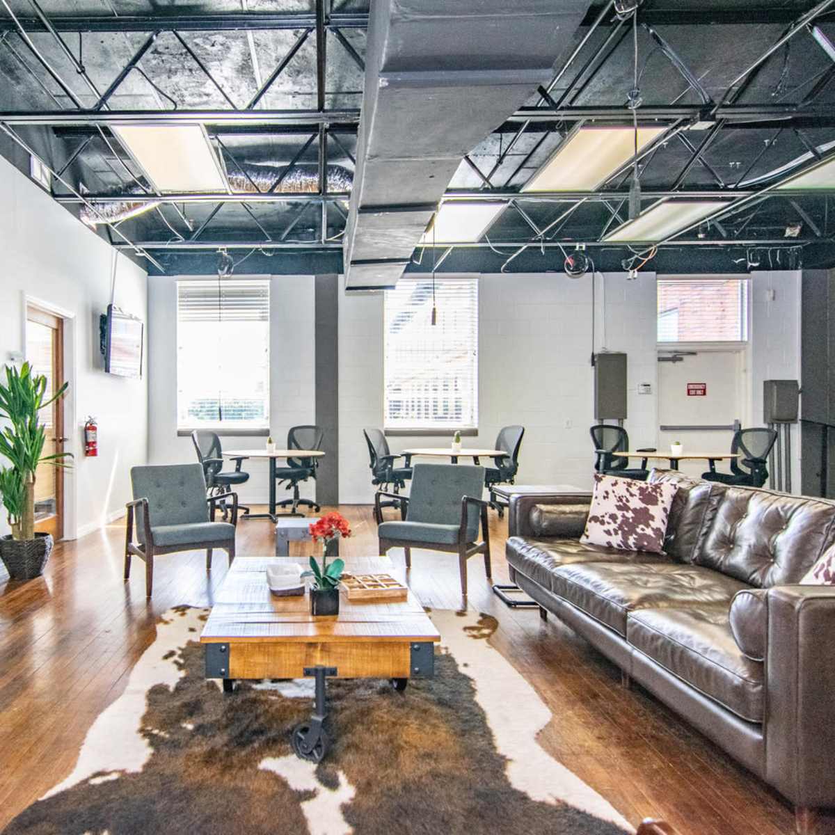 A modern office lounge area with a leather sofa, a coffee table, and a few workstations in the background.