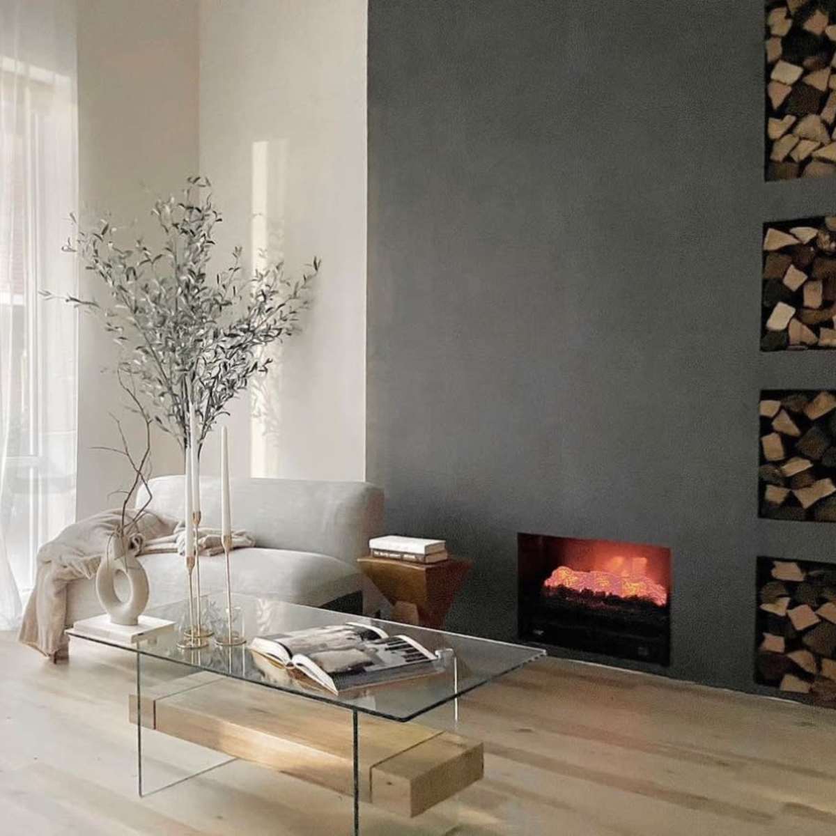 A living room features a glass coffee table, a sofa, a decorative plant, a fireplace, and large sheer curtains.