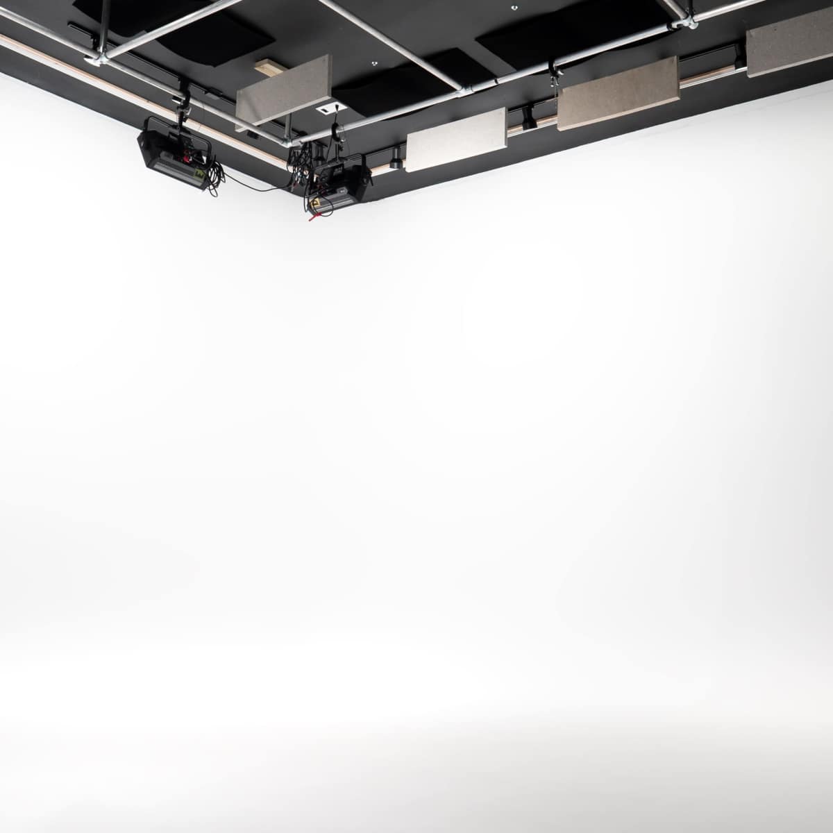 A minimalist photo studio with a white backdrop and suspended lighting equipment.
