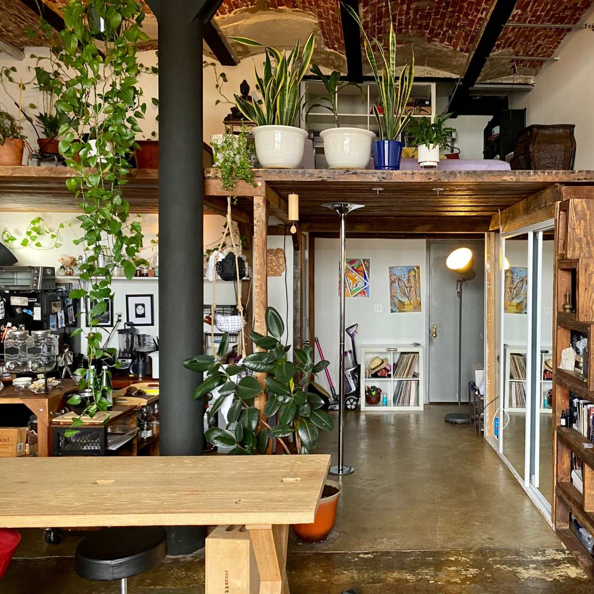 A modern interior space featuring a wooden loft area with plants, a set of stairs, and a coffee station on the left side.