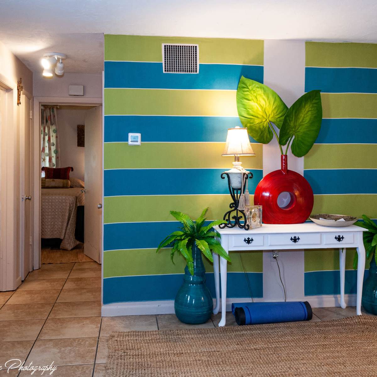 A brightly colored entryway featuring a green and blue striped wall, a white console table with a lamp, decorative plants, and a red circular artwork.