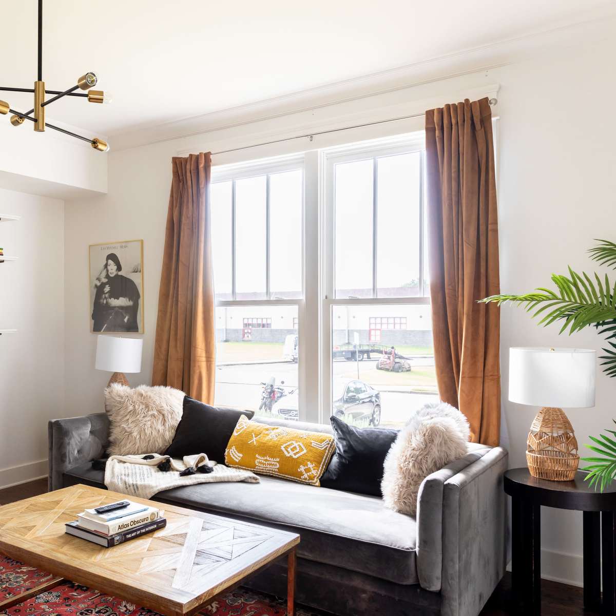 A modern living room featuring a gray sofa with decorative pillows, a wooden coffee table, and a large window with curtains, complemented by shelves displaying various items.
