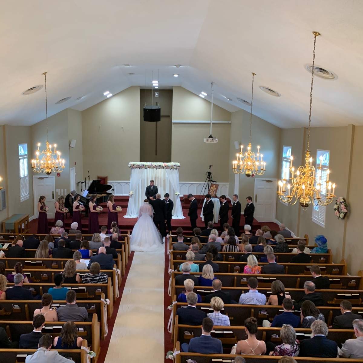 A wedding ceremony is taking place in a church filled with seated guests, while the bridal couple stands at the altar surrounded by attendants.