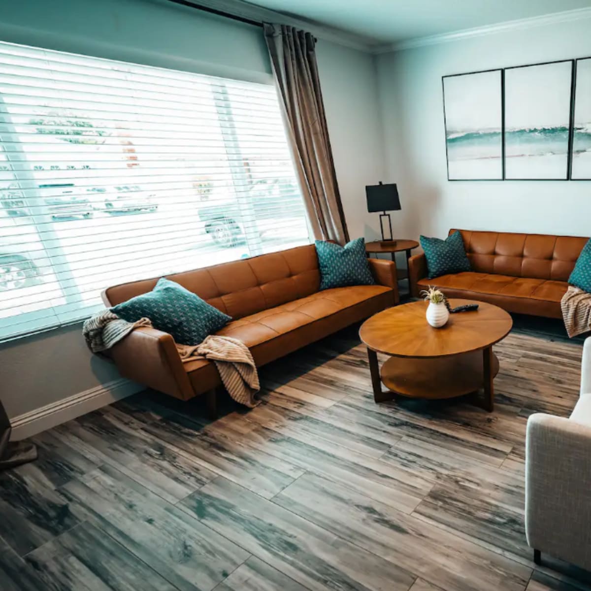 A modern living room features brown leather sofas, a round wooden coffee table, and white armchairs, with large windows providing natural light.