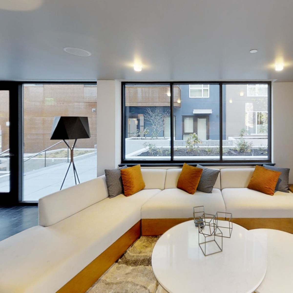 A modern lounge area with a large sectional sofa, a round coffee table, and a window view of an outdoor space.