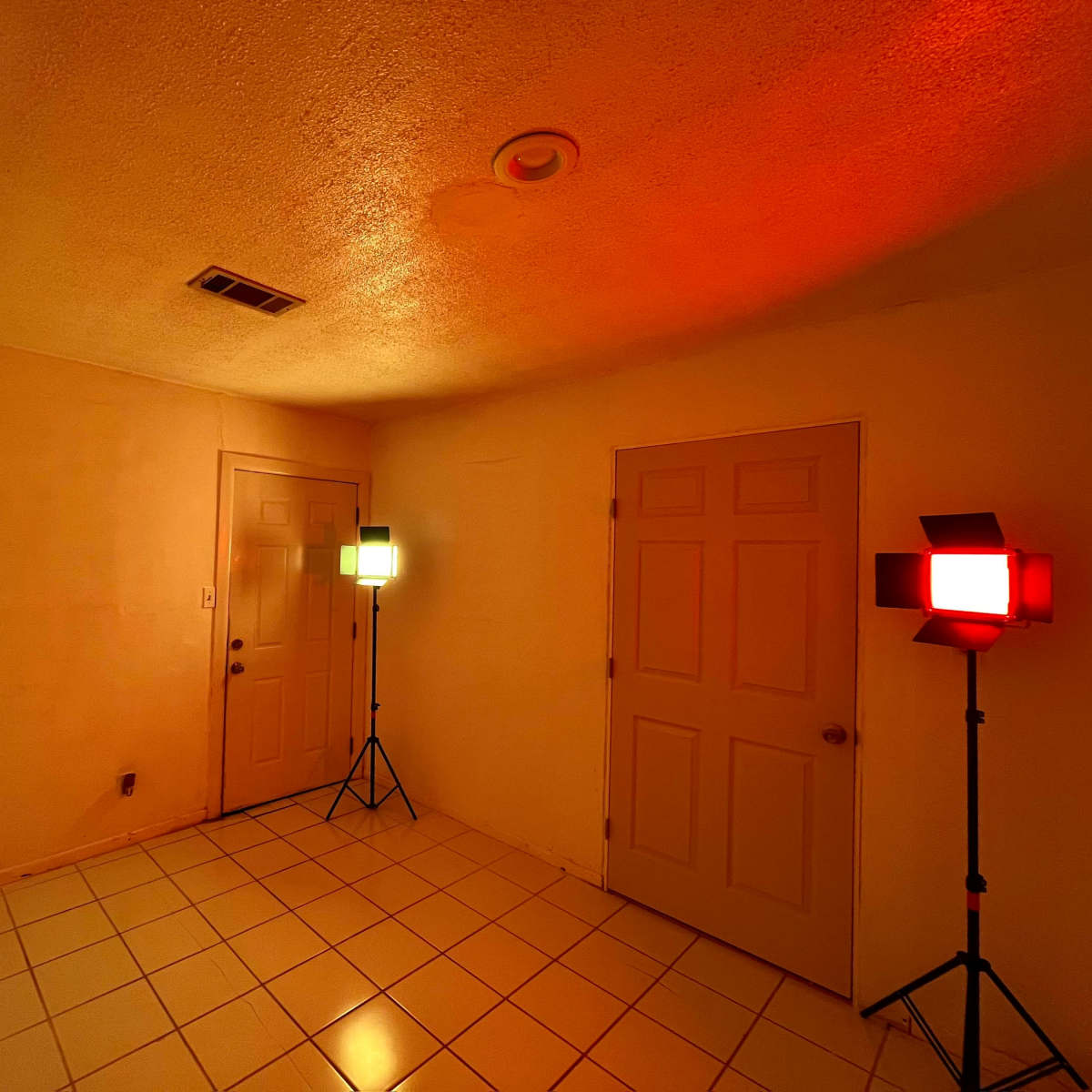 A dimly lit room with two colored light stands, one red and one green, positioned near two closed doors.
