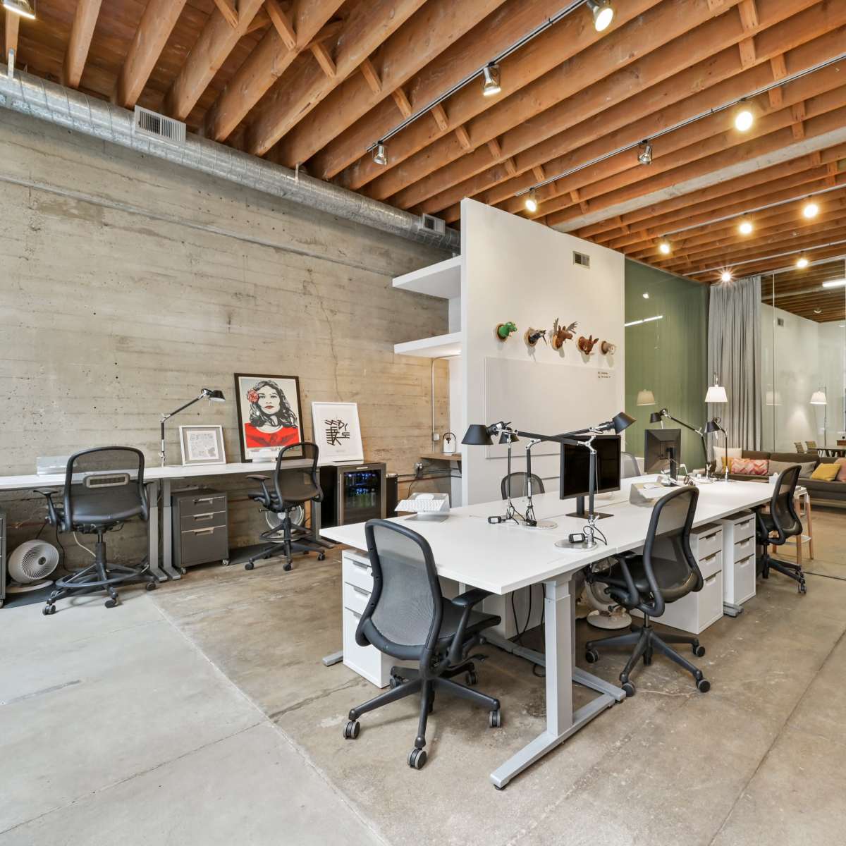 A modern office space with exposed wooden beams, multiple workstations equipped with desks and office chairs, and a spiral staircase leading to an upper level.