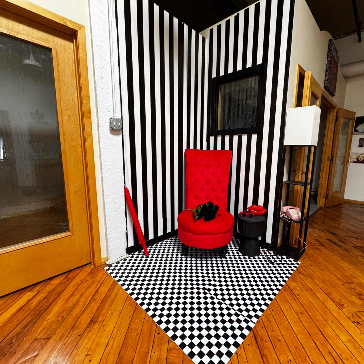 A red chair with tufted upholstery is positioned in a corner with black and white striped walls and a checkered floor.