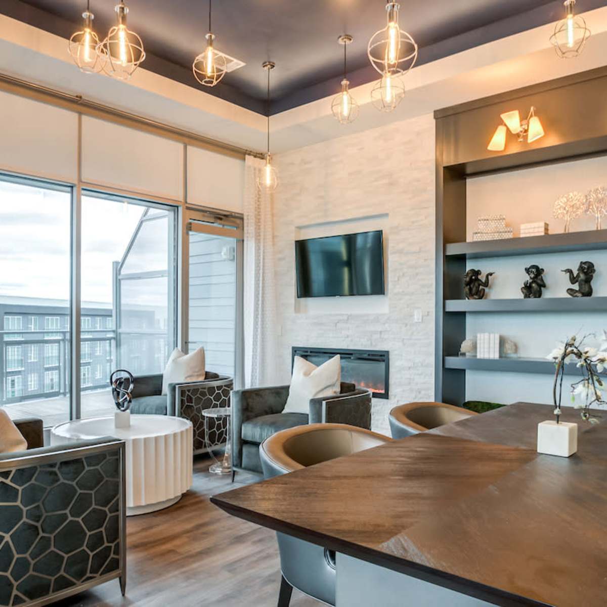 A modern lounge area with four chairs arranged around a coffee table, large windows, and a wall-mounted television.