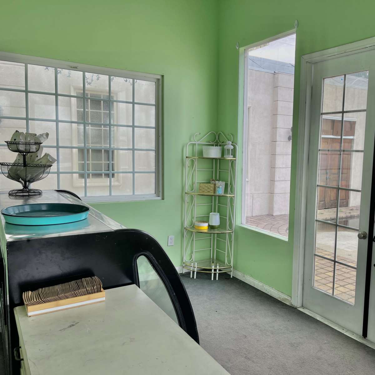 A green-walled room with large windows, double glass doors, and a white shelf containing various items.